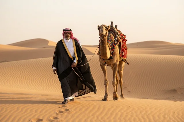رجل سعودي مع جمل في الصحراء بالزي التقليدي والبشت