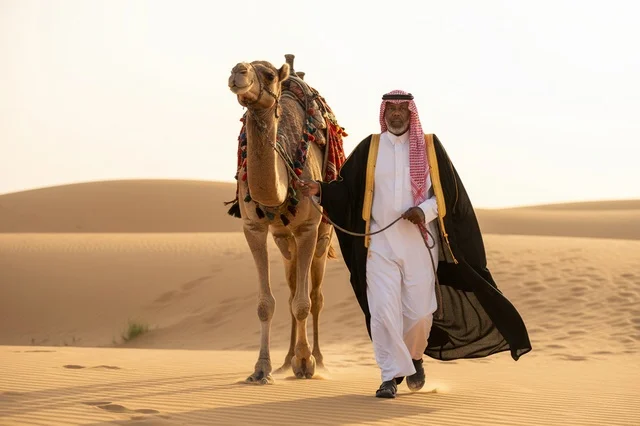 رجل سعودي مع جمل في الصحراء وقت الغروب