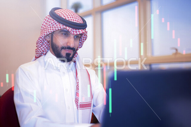 صورة لرجل عربي خليجي سعودي مبتسم في مقر عمله بالشركة يستخدم الحاسوب مدموجة برسوم بيانية خاصة بصعود و هبوط البورصة المالية ثلاثية الأبعاد بتقنية الهولوجرام ، الإستثمار المالي و الإقتصادي ، مشاريع و أعمال إلكترونية تجارية