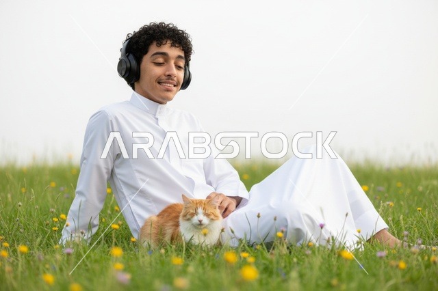 شاب سعودي بالثوب مع قطة في حقل عشبي