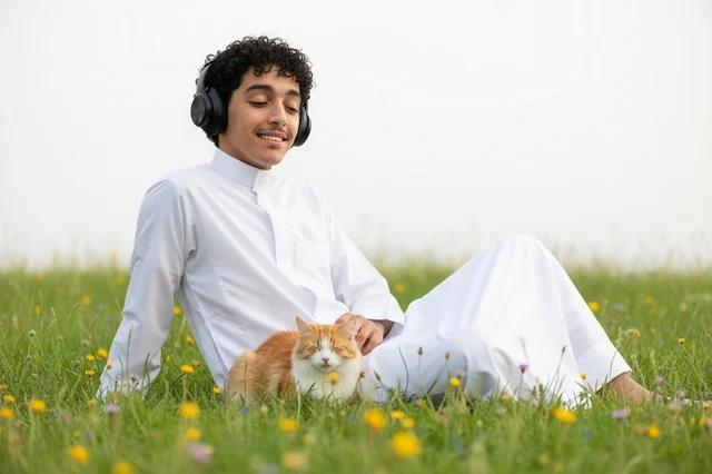 شاب سعودي بالثوب مع قطة في حقل عشبي