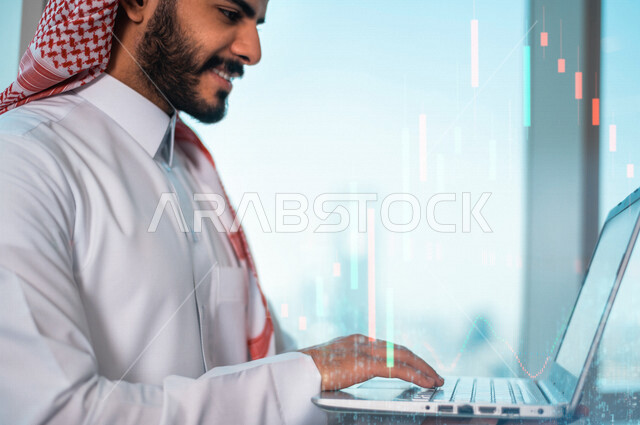 صورة لرجل عربي خليجي سعودي مبتسم في مقر عمله بالشركة يستخدم الحاسوب مدموجة برسوم بيانية خاصة بصعود و هبوط البورصة المالية ثلاثية الأبعاد بتقنية الهولوجرام ، الإستثمار المالي و الإقتصادي ، مشاريع و أعمال إلكترونية تجارية