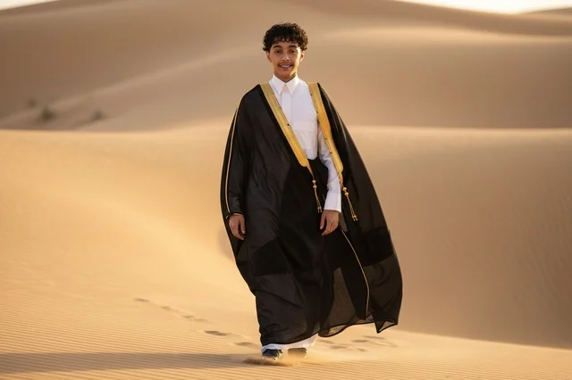 Saudi Boy in Traditional Bisht Walking on Desert Dunes