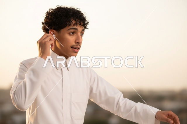 شاب سعودي بالثوب الأبيض يستخدم سماعات لاسلكية
