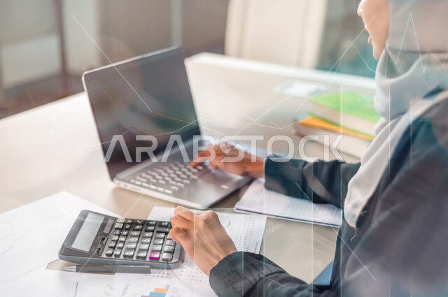 موظفة أنظمة بنكية و قواعد بيانات عربية سعودية خليجية تستخدم الآلة الحاسبة و جهاز الحاسوب لتصنيف و تسجيل المعلومات المالية مدموجة بخلفية لعملات نقدية و رسومات بيانية لصعود و هبوط البورصة المالية ، وظيفة المحاسبة في البنوك