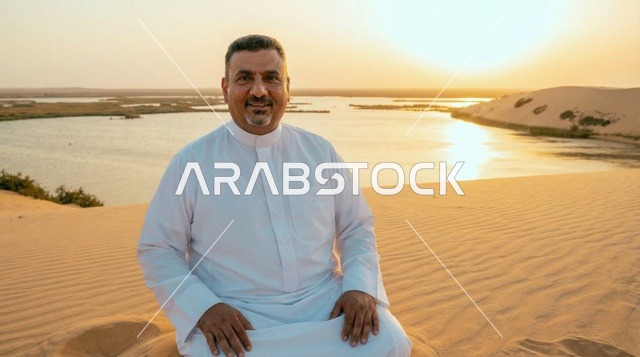 رجل سعودي بالثوب التقليدي عند بحيرة صحراوية وقت الغروب