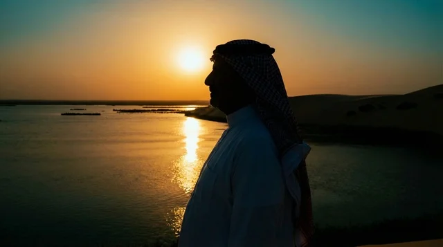 رجل سعودي بالزي التقليدي عند بحيرة صحراوية وقت الغروب
