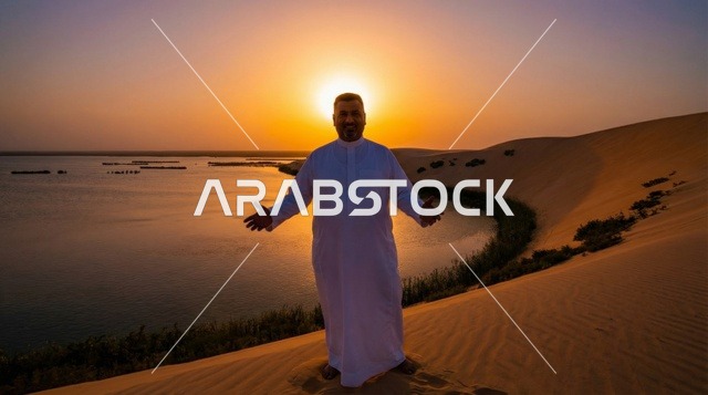 رجل سعودي بالثوب عند بحيرة صحراوية وقت الغروب