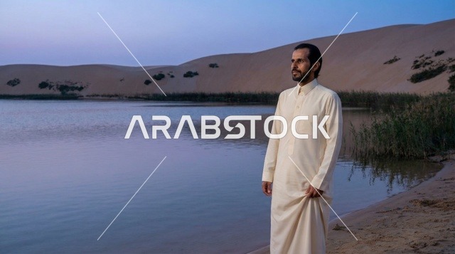رجل سعودي بالثوب في بحيرة صحراوية وقت الغسق