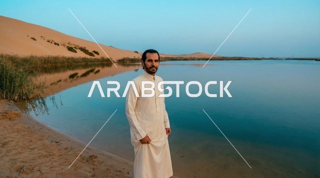 رجل سعودي بالثوب بجانب بحيرة صحراوية