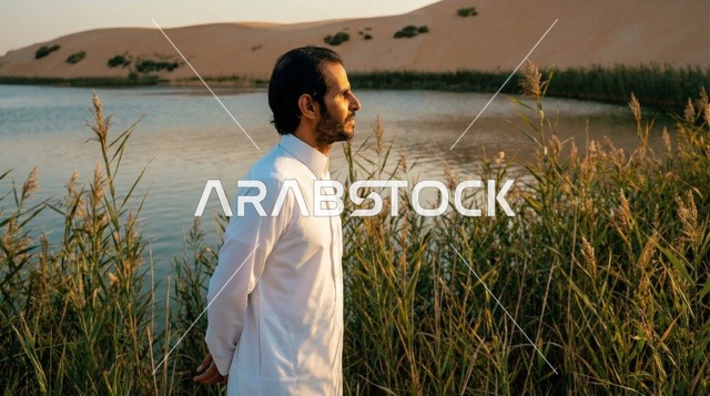 رجل سعودي بالثوب التقليدي عند بحيرة صحراوية وقت الغروب