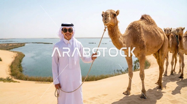 رجل سعودي مع الإبل عند بحيرة صحراوية