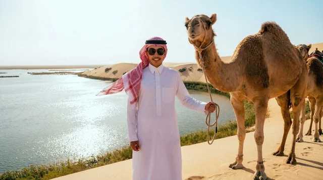 رجل سعودي مع جمل بجوار بحيرة في الصحراء