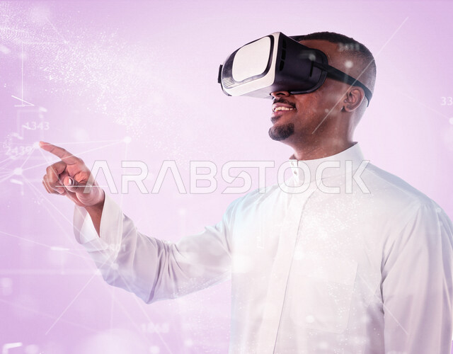 رجل عربي خليجي سعودي مبتسم يرتدي نظارة الواقع الإفتراضي ثلاثية الأبعاد ، يضغط بأصبع السبابة تجاه نقاط توصيل على شبكة هولوجرامية بالواقع الإفتراضي ، إستخدام حاسة اللمس لتحريك العناصر الهولوجرامية ، محاكاة العالم الافتراضي ، رموز رقمية الكترونية