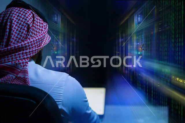 صورة من الخلف لرجل عربي خليجي سعودي يجلس أمام الحاسوب ، يعمل في مركز بيانات و يقوم بإدارة الخوادم باستخدام الجهاز التقني الحاسوب ، إدارة خوادم الانترنت و السيرفرات ، حظيرة خوادم ، تقنيات و تكنولوجيا ، مركز البيانات داتا سنتر 