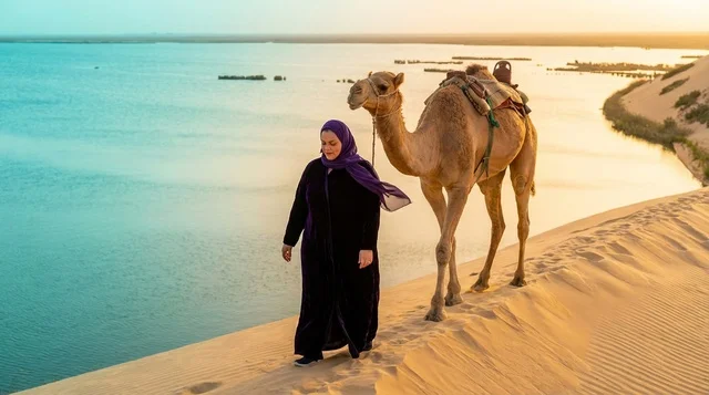 امرأة عربية مع جمل على الكثبان الرملية وقت الغروب
