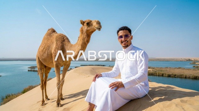 رجل سعودي بالثوب مع جمل عند بحيرة صحراوية