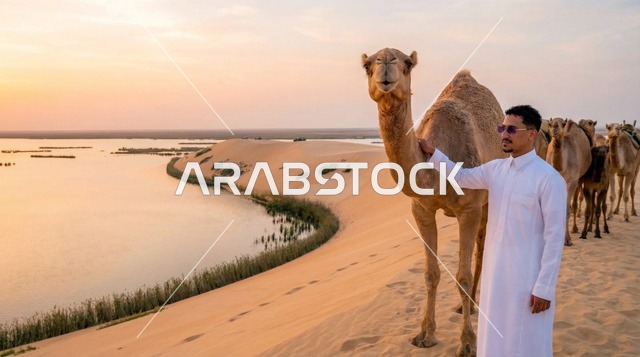 رجل سعودي مع الإبل عند بحيرة صحراوية وقت الغروب