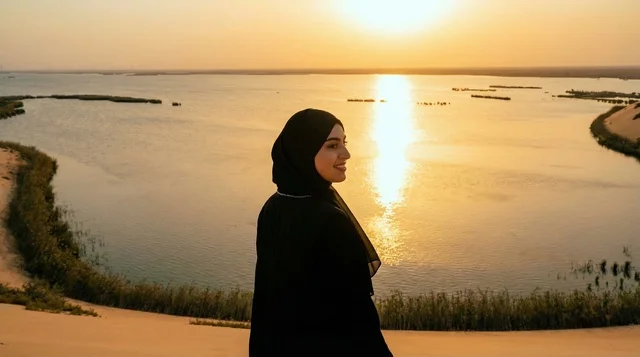 امرأة سعودية بالعباءة عند بحيرة صحراوية وقت الغروب