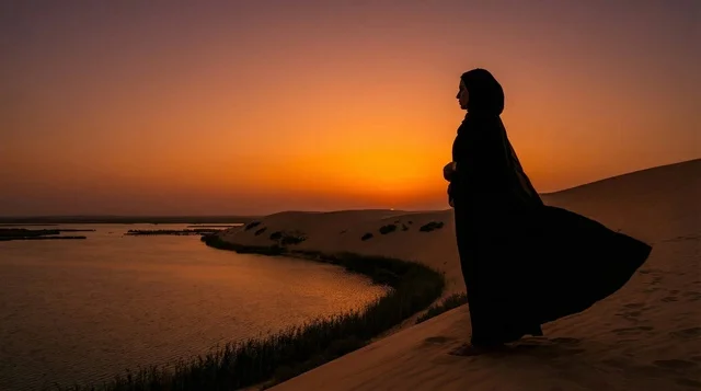 امرأة سعودية بالعباءة فوق الكثبان الرملية وقت الغروب