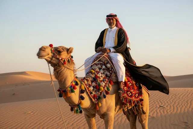 رجل سعودي يركب الجمل في الصحراء وقت الغروب