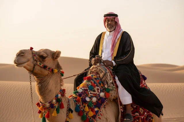 رجل سعودي فوق جمل في الصحراء وقت الغروب