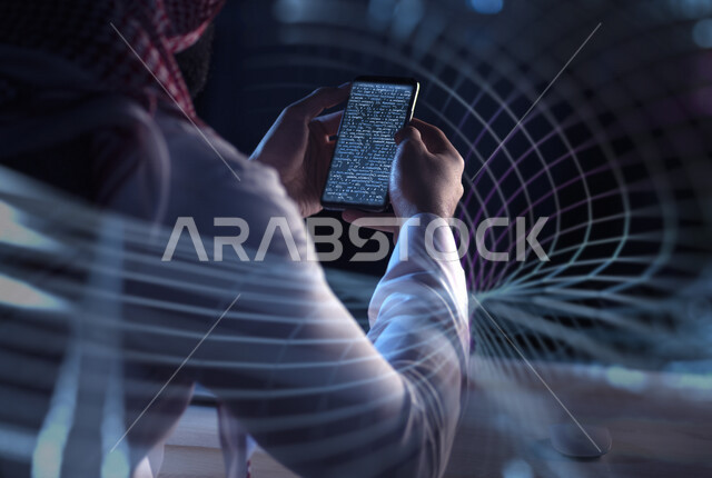 صورة من الخلف لرجل عربي  خليجي سعودي يحمل هاتف محمول يقوم بعملية تشفير لقواعد البيانات ، استخدام الخوارزميات لتحويل النصوص و البيانات إلى بيانات مشفرة ، مطور يعمل على تطوير و بناء المواقع والتطبيقات الالكترونية 