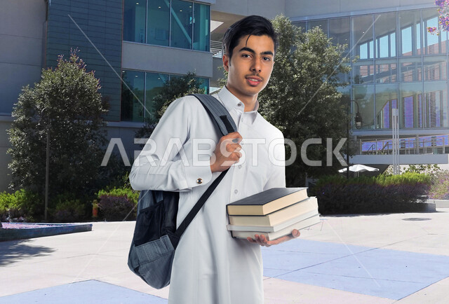 صورة طالب جامعي عربي خليجي سعودي يرتدي الثوب السعودي التقليدي ، يمسك بيده الكتب الجامعية للدراسة ، التعلم الذاتي , الجد والإجتهاد , مرحلة دراسية , التعلم الأكاديمي , العودة إلى المدارس . 