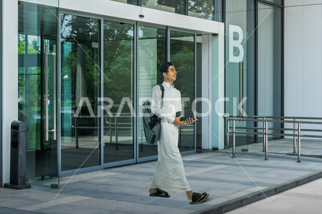 صورة طالب جامعي عربي خليجي سعودي يرتدي الثوب السعودي التقليدي ، يمسك بيده الكتب الجامعية للدراسة ، التعلم الذاتي , الجد والإجتهاد , مرحلة دراسية , التعلم الأكاديمي , العودة إلى المدارس . 