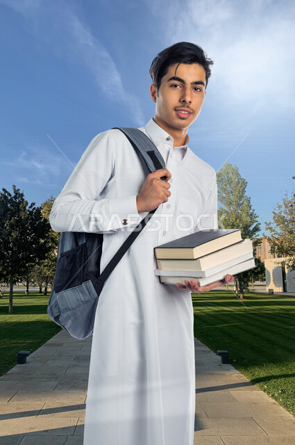 صورة لتلميذ جامعي عربي خليجي سعودي يرتدي الثوب السعودي التقليدي ، يمسك بيده الكتب الجامعية للدراسة ، ايماءات و تعابير للوجه و اليدين مختلفة ، تأدية الواجبات ، التعلم الذاتي , الجد والإجتهاد , التعليم الأكاديمي , الذهاب للجامعة . 