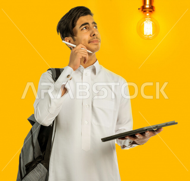 صورة لطالب جامعي عربي خليجي سعودي يرتدي الثوب السعودي التقليدي ، يمسك بيده جهاز التابلت للتعلم ، ايماءات التفكير , رؤية مستقبلية ، أفكار إبداعية تطويريه , مفهوم الفكرة مع الإبتكار والإلهام , تحقيق الإنجازات والإبتكارات , براءة الإختراع , المصباح الكهربائي