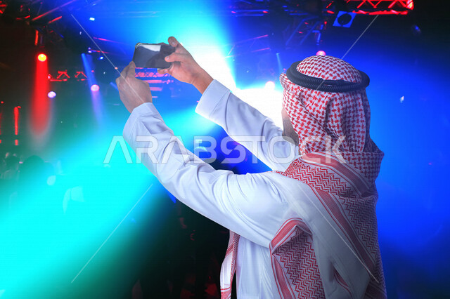 A picture of a Saudi Arabian Gulf man taking a memorial photo through a mobile phone at the Middle East Festival, front camera, enjoying leisure time, summer vacation, Riyadh season, amusement and entertainment, spending good time, tourism in the Kingdom 