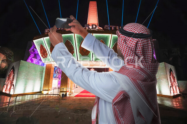 صورة لرجل عربي خليجي سعودي يقوم بالتقاط صورة تذكارية من خلال الهاتف المحمول في بوليفارد الرياض ، كاميرا امامية ، الاستمتاع بوقت الفراغ , اجازة صيفية , موسم الرياض , ملاهي وترفيه , قضاء وقت ممتع , السياحة في المملكة العربية السعودية .