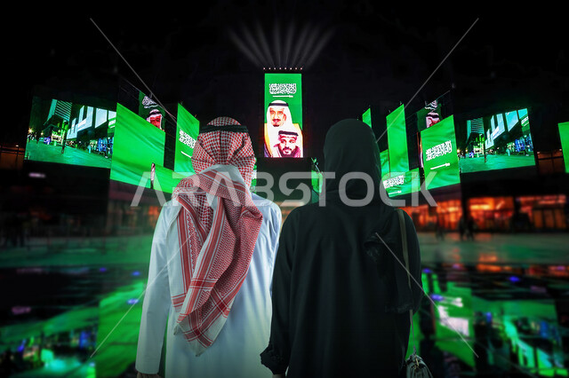 زوجان عربيان سعوديان خليجيان يقضيان وقتا ممتعا في بوليفارد الرياض , موسم الرياض , شاشات كبيرة مضاءة في بوليفارد الرياض , اختيار المكان المناسب لقضاء وقت الفراغ , الإجازة الصيفية , تسلية وترفيه , السياحة في المملكة العربية السعودية .