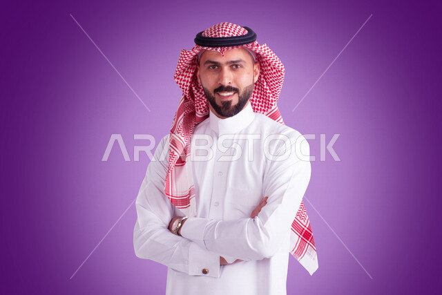بورتريه لرجل عربي سعودي خليجي متكتف اليدين يرتدي الثوب الأبيض والشماغ السعودي, الوقوف بإستقامه, ايماءات وجه تدل على السعاده والبهجه, الثقه بالنفس