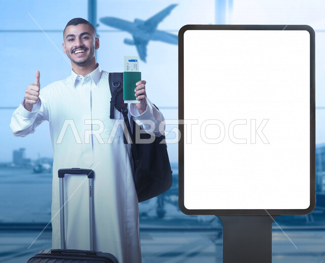 شاب عربي خليجي سعودي مبتسم مع حقيبة سفر ، يقف بجانب لوحة يونيبول إعلانية تجارية مضيئة بيضاء في قاعة في المطار ، يحمل بيده جواز سفر و يشير باليد الأخرى بأصبع الابهام للعمل الممتاز ، رحلة سياحية تعليمية ، رحلة عمل ، إعلانات دعائية و تسويقية ، موك أب لوحة إع