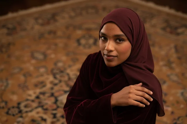 Muslim Woman in Maroon Hijab on Traditional Carpet