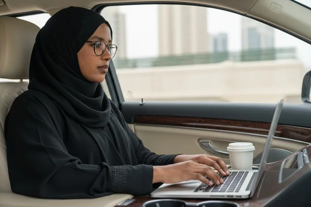 سيدة أعمال إماراتية تعمل على الكمبيوتر المحمول في السيارة
