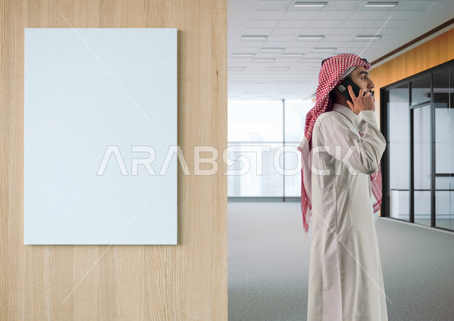 A Saudi Arabian Gulf man standing next to a white business Unipole billboard in the company talking on mobile phone making advertising business deals remote work management e-marketing mok up billboard