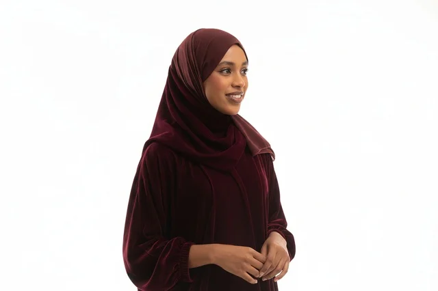 امرأة بعباءة مخملية خمرية وحجاب خلفية بيضاء