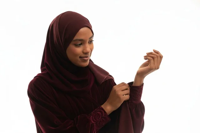 امرأة بعباءة مخملية خمرية وحجاب خلفية بيضاء