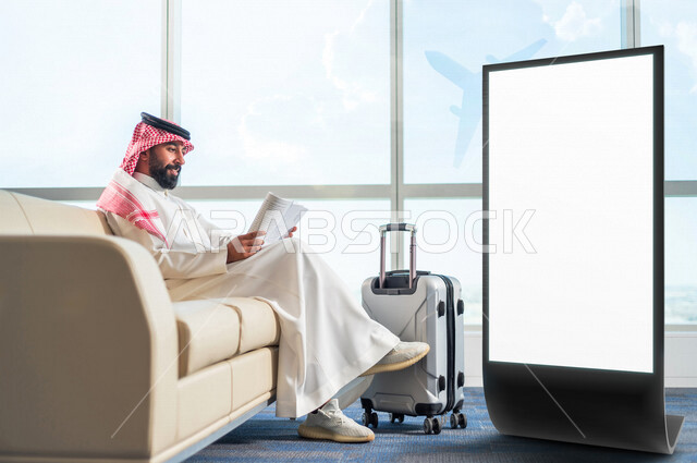 رجل عربي خليجي سعودي مبتسم يجلس في  قاعة الانتظار بجانب لوحة يونيبول إعلانية تجارية مضيئة بيضاء ، حجز تذاكر الطيران و الفنادق ، تسويق شركات الطيران ، رحلة سياحية ، رحلة عمل ، عروض تسويقية جوية ، موك أب لوحة إعلانية 