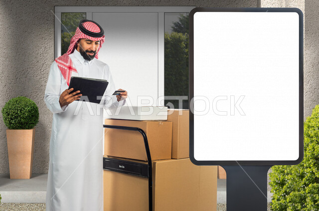 رجل عربي سعودي خليجي يقوم بتوصيل الطلبات والبضائع للزبائن ، تأكيد الحجوزات عبر جهاز التابلت ، بجانبه لوحة يونيبول إعلانية تجارية مضيئة بيضاء ، عروض تسويقية لخدمات طلبات التوصيل ، إعلانات دعائية ، موك أب لوحة إعلانية 