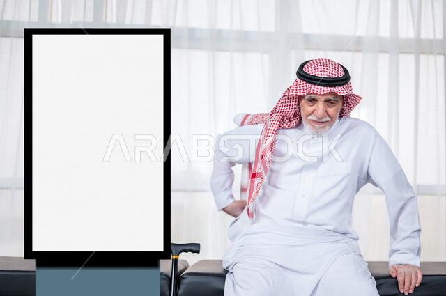 An elderly Saudi Arabian Gulf man puts his hand on his back suffering from aches and pains, medical examination and provision of services and medical care, white illuminated commercial Unipol billboard, medical advertisements, mock-up billboard