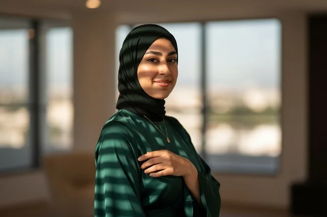 امرأة عربية مبتسمة ترتدي الحجاب والعباءة الخضراء في الداخل