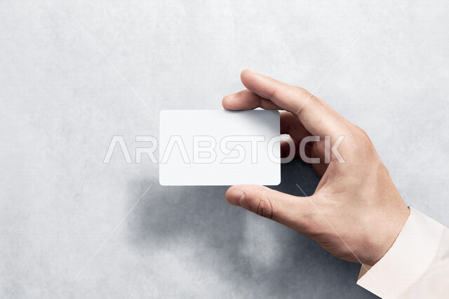 Close-up photography of the hand of a Saudi Arabian Gulf man holding a blank white card, personal business card, identification card, personal badge, personal identification, plastic card
