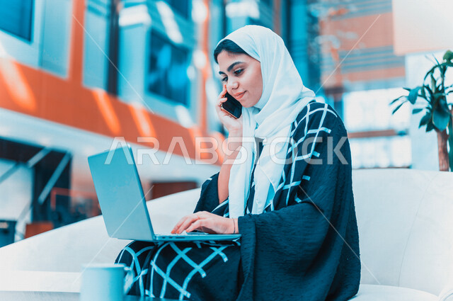 A Saudi Arabian Gulf woman using a laptop computer and making a phone call, professional computer and information technology jobs, e-marketing, surfing the Internet, remote work, e-learning