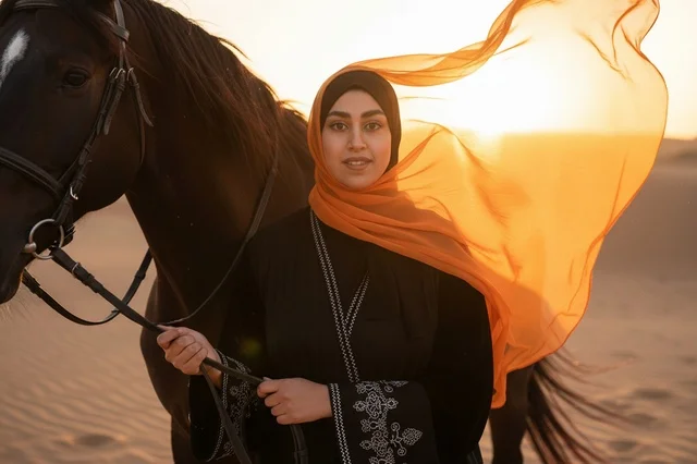 امرأة إماراتية مع خيل عربي في غروب الصحراء