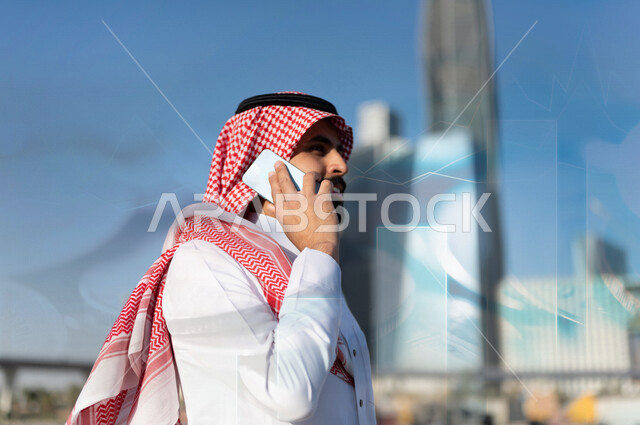 رجل اعمال عربي خليجي سعودي مبتسم يقوم باجراء مكالمة هاتفية مع خلفية مدموجة بالعملات المعدنية والرسم البياني لسوق الاوراق المالية ، مناقشة النمو والارباح المالية ، ادخار وتوفير الاموال ، ادارة الاعمال والاستثمار