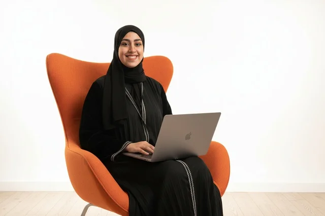 امرأة إماراتية مع حاسوب محمول على كرسي برتقالي